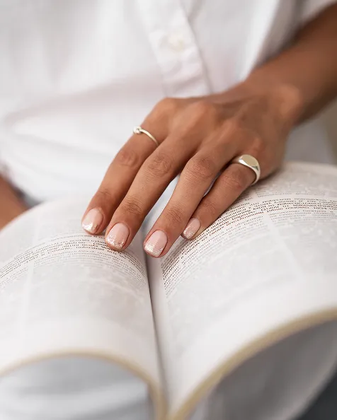Une main posée sur un livre ouvert, portant une bague.