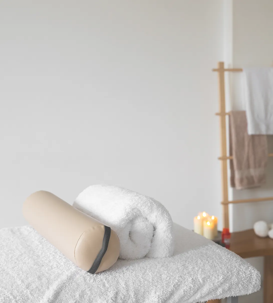 Une serviette roulée et des accessoires de spa posés sur un lit, ambiance apaisante.